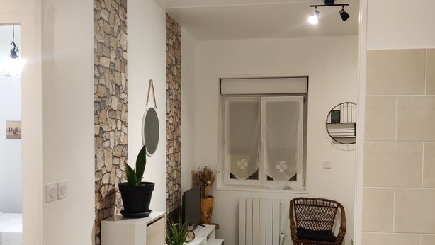 Un espai vital compacte amb zona de cuina, un racó de menjador i una zona d'estar amb una cadira de vimet.