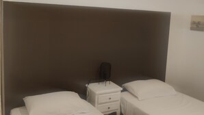 Una habitació d'hotel amb dos llits individuals, una nitzeta amb una làmpada i un llum penjant a la paret.