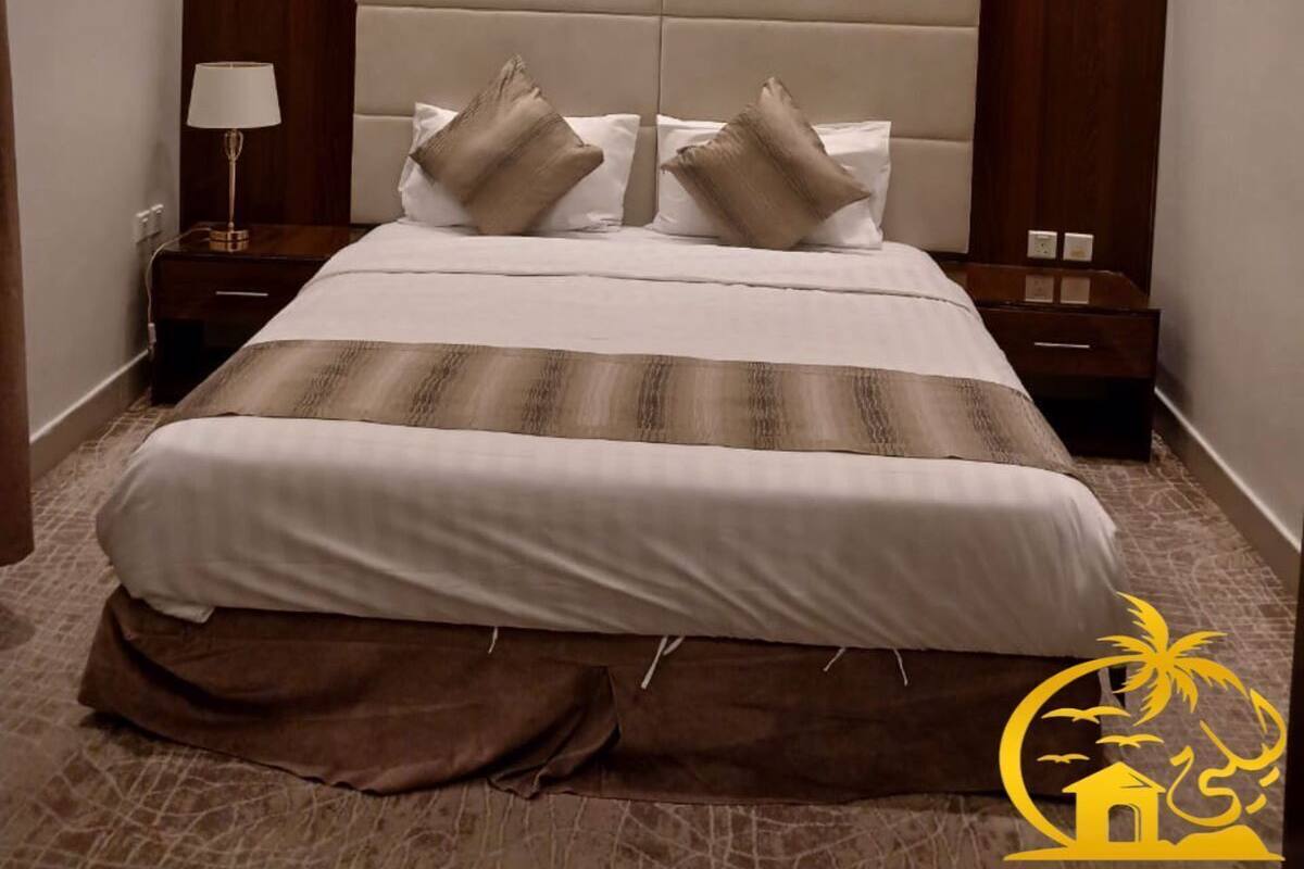 Una habitación de hotel moderna con una cama grande, dos mesitas de noche, una lámpara de techo y un cabecero de madera.