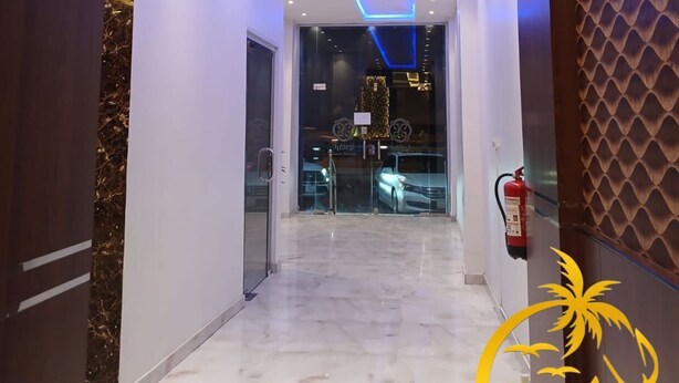 Un pasillo moderno de hotel con piso de mármol, iluminación empotrada y una puerta de cristal que da a un estacionamiento.