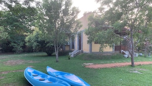 Deux kayaks bleus sur une pelouse verdoyante, avec des arbres et un bâtiment en arrière-plan.