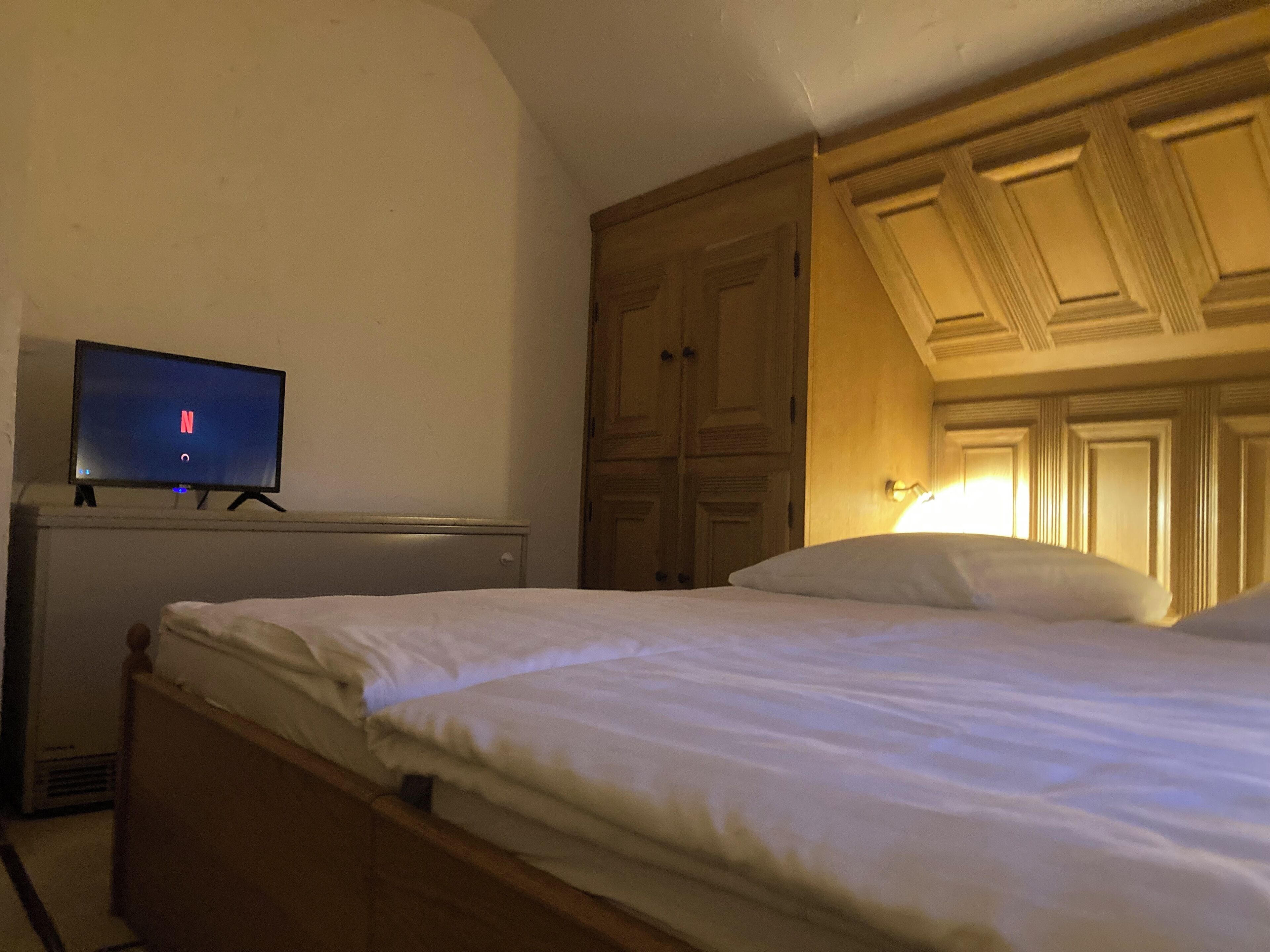 Een slaapkamer met een bed, een televisie op een dressoir en een kledingkast.