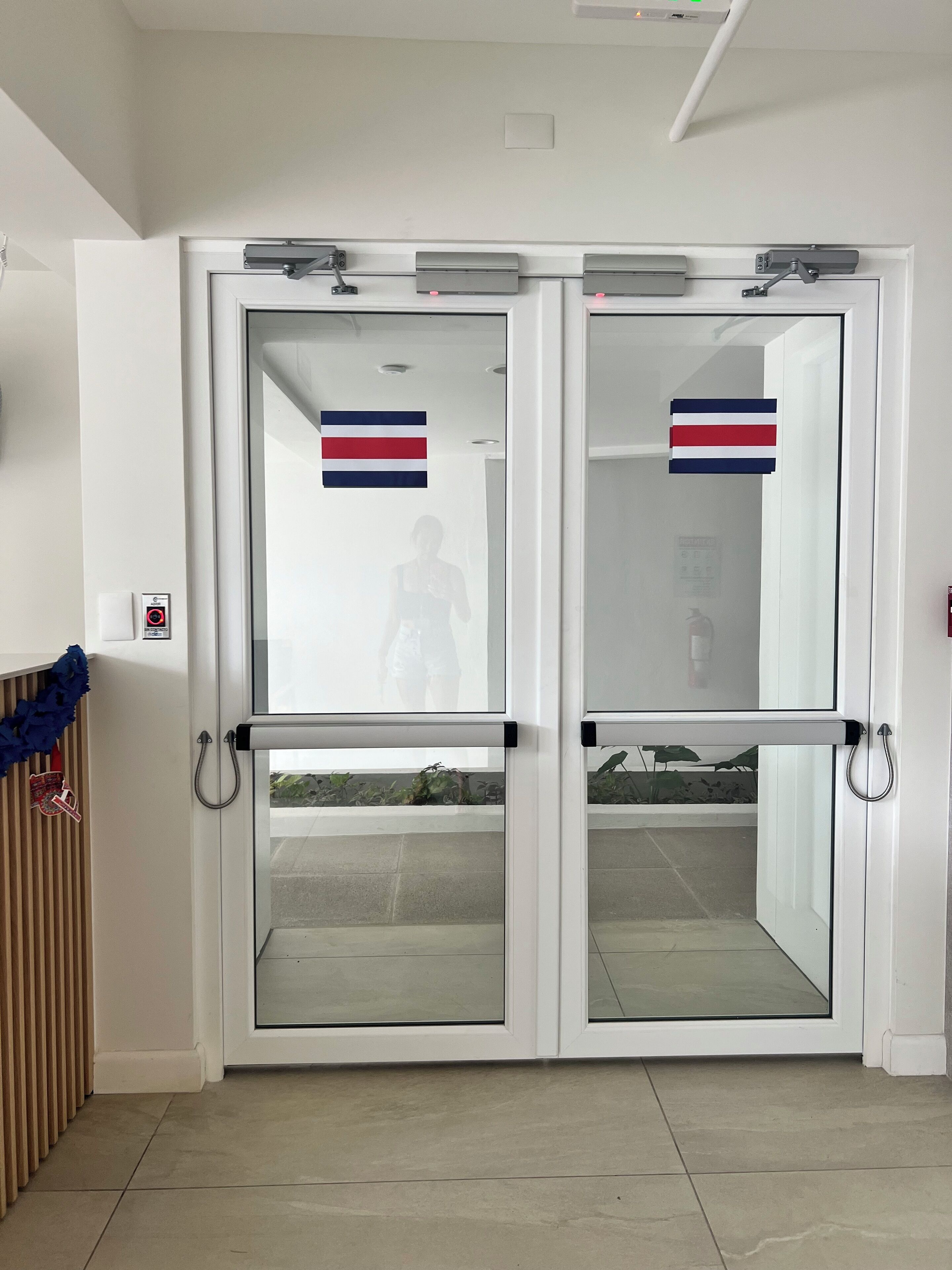 A set of double doors with glass panels, each door has a Thai flag, and there is a security intercom on the left door.