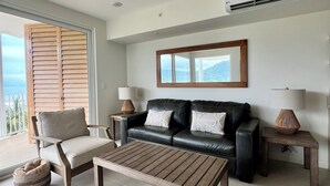 A modern living room with a black leather sofa, wooden coffee table, and a view of the outdoors.