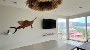 A modern kitchen with a large island, a mounted TV, and a view of the city through large windows.