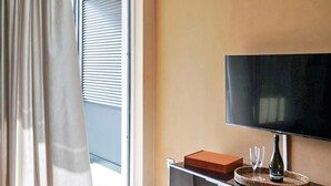 Ett modernt vardagsrum med en platt-TV, en soffa, ett soffbord och en skjutdörr i glas som leder ut till en balkong.
