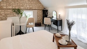 A bedroom with a sloped ceiling, a stone wall, a bed, a desk, a chair, a dresser, a mirror, and a window with sheer curtains. - Justaura Retreat Cosy Barn in Quiet Private Area (Lincoln)