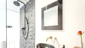 A modern bathroom with a glass shower enclosure, a black vessel sink, and a large mirror.