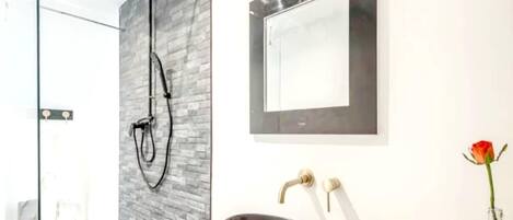 A modern bathroom with a glass shower enclosure, a black vessel sink, and a large mirror.