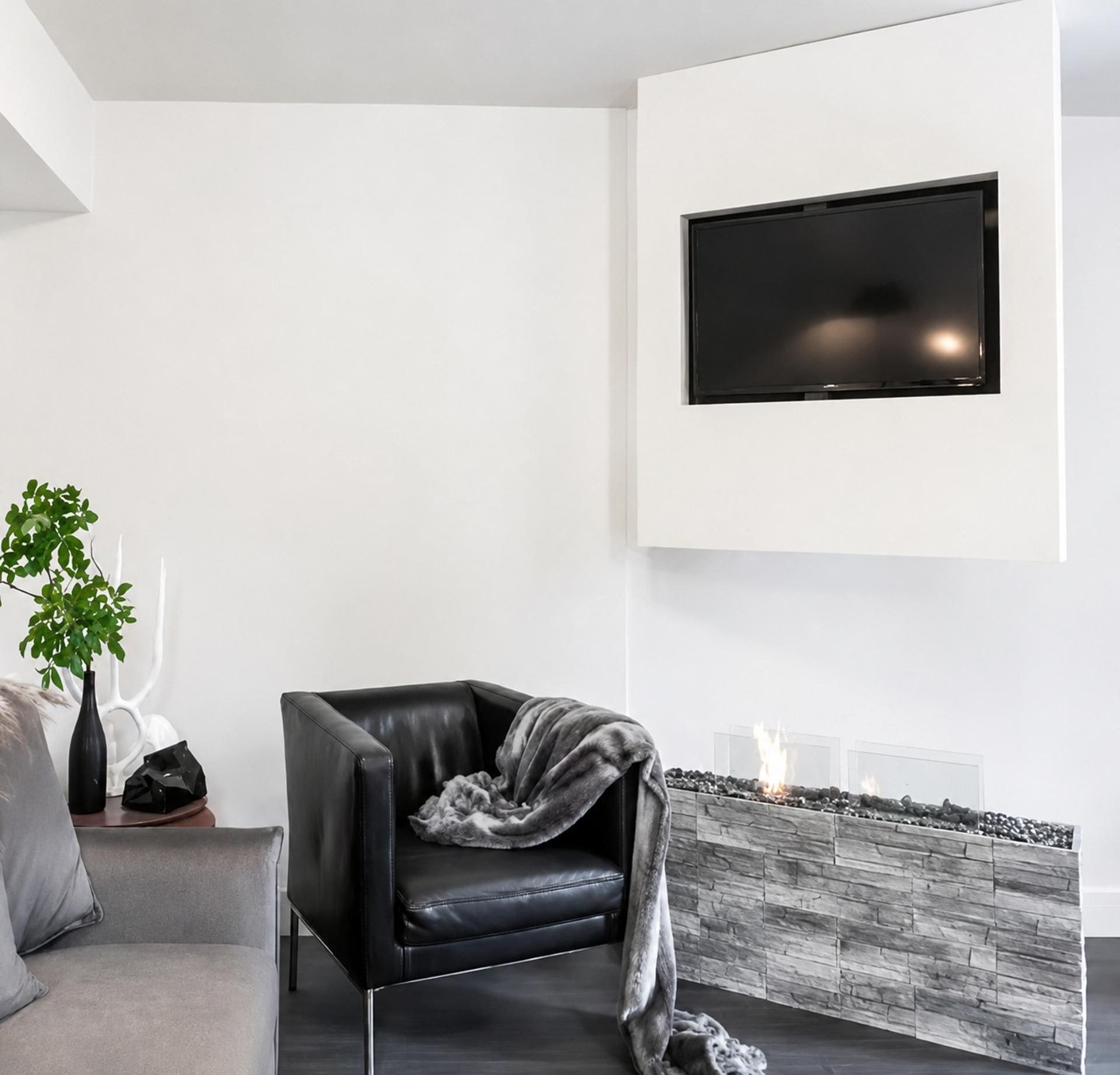Una sala de estar moderna con un sillón de cuero negro, un televisor de pantalla plana montado en la pared y una chimenea con textura de piedra.