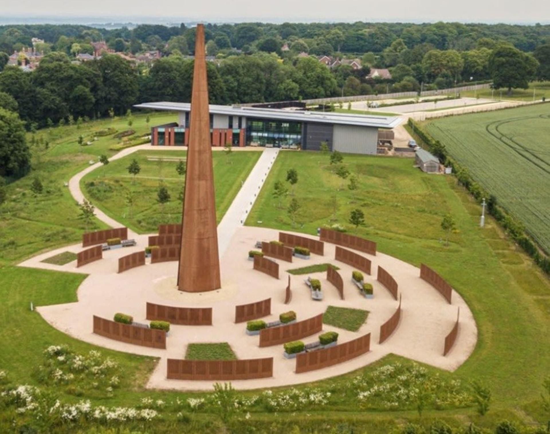 A modern building with a tall central tower, surrounded by a landscaped area with pathways and benches.