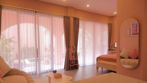 A spacious room with a large bed, a sofa, a small table, and a chair. There are curtains on the windows, and a mirror on the wall. - PONDER Bali (Canggu)