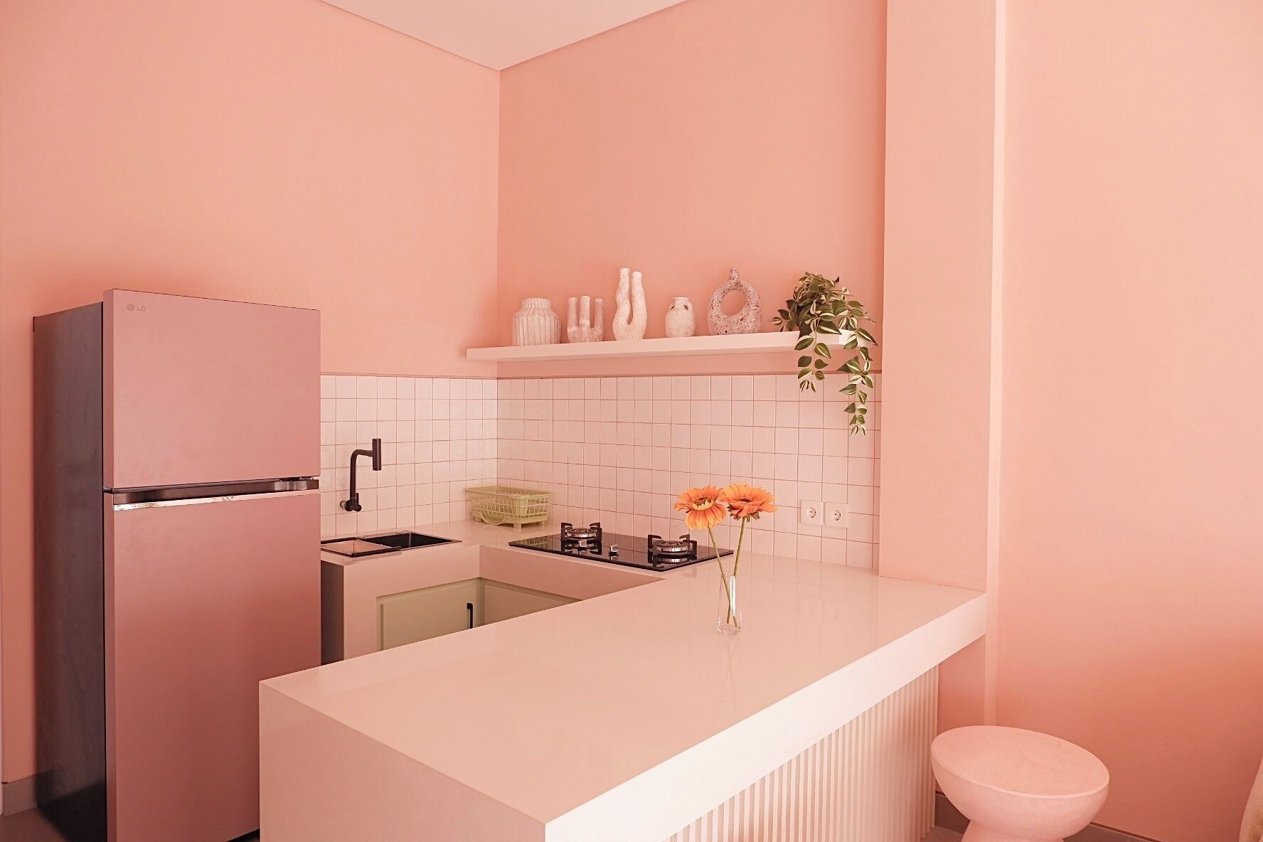 Una cocina moderna con un refrigerador rosa, encimera blanca y un lavamanos pequeño.