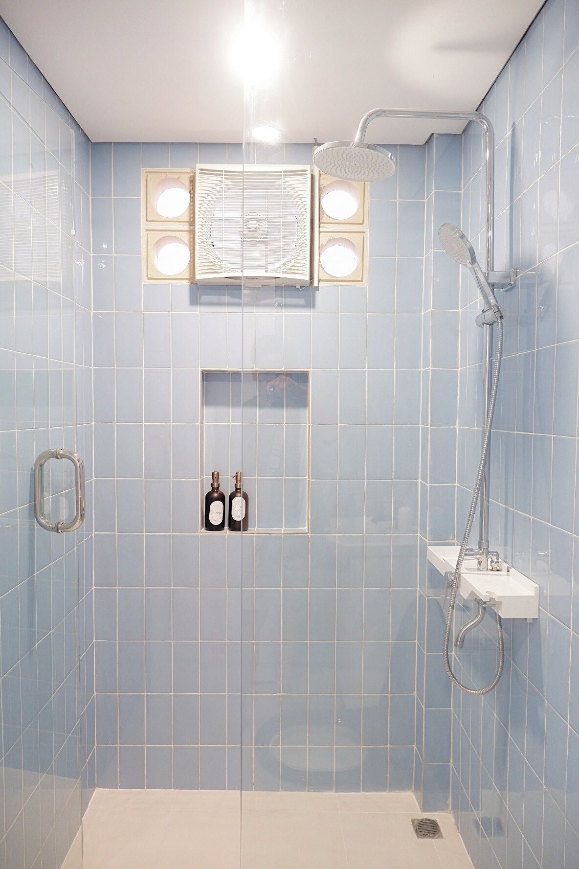 Ein Badezimmer mit blauen Fliesen, einer Dusche, einem Waschbecken und zwei Shampoo-Flaschen.