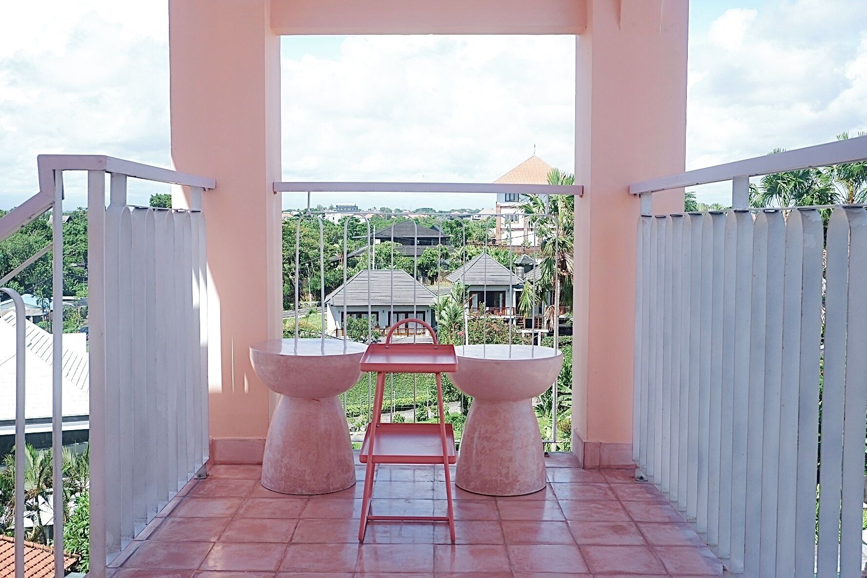 Un balcon avec une table et des chaises, une vue sur les bâtiments et la verdure, et une balustrade blanche.