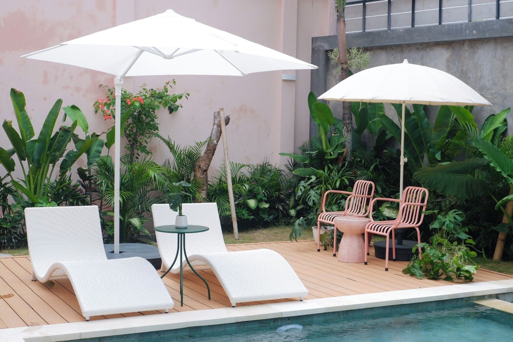 A poolside area with white lounge chairs, a small round table, and two white umbrellas providing shade.