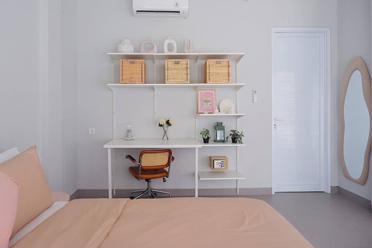 A bedroom with a bed, a desk with shelves, a chair, and a door.