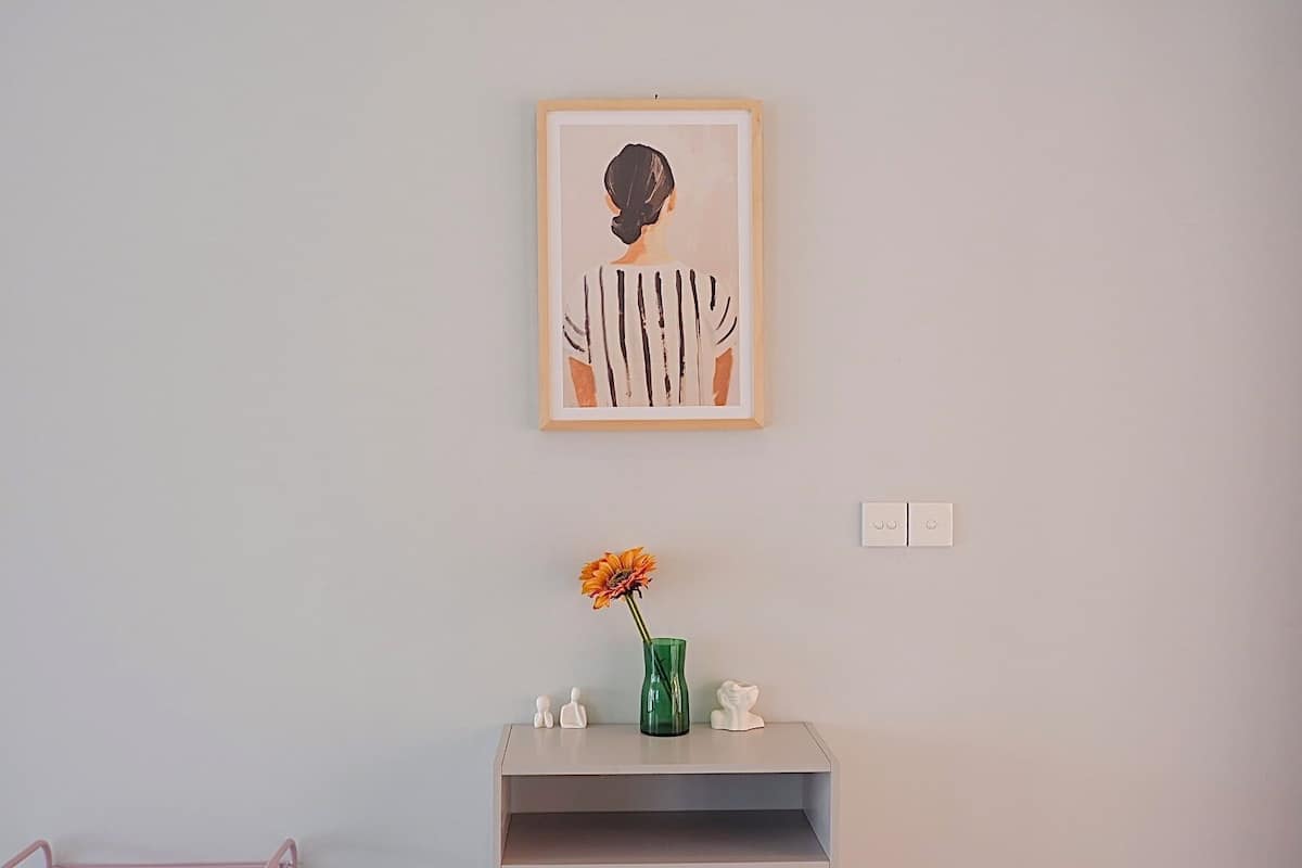 A framed artwork on a wall, a vase with a flower, and a small shelf with figurines.