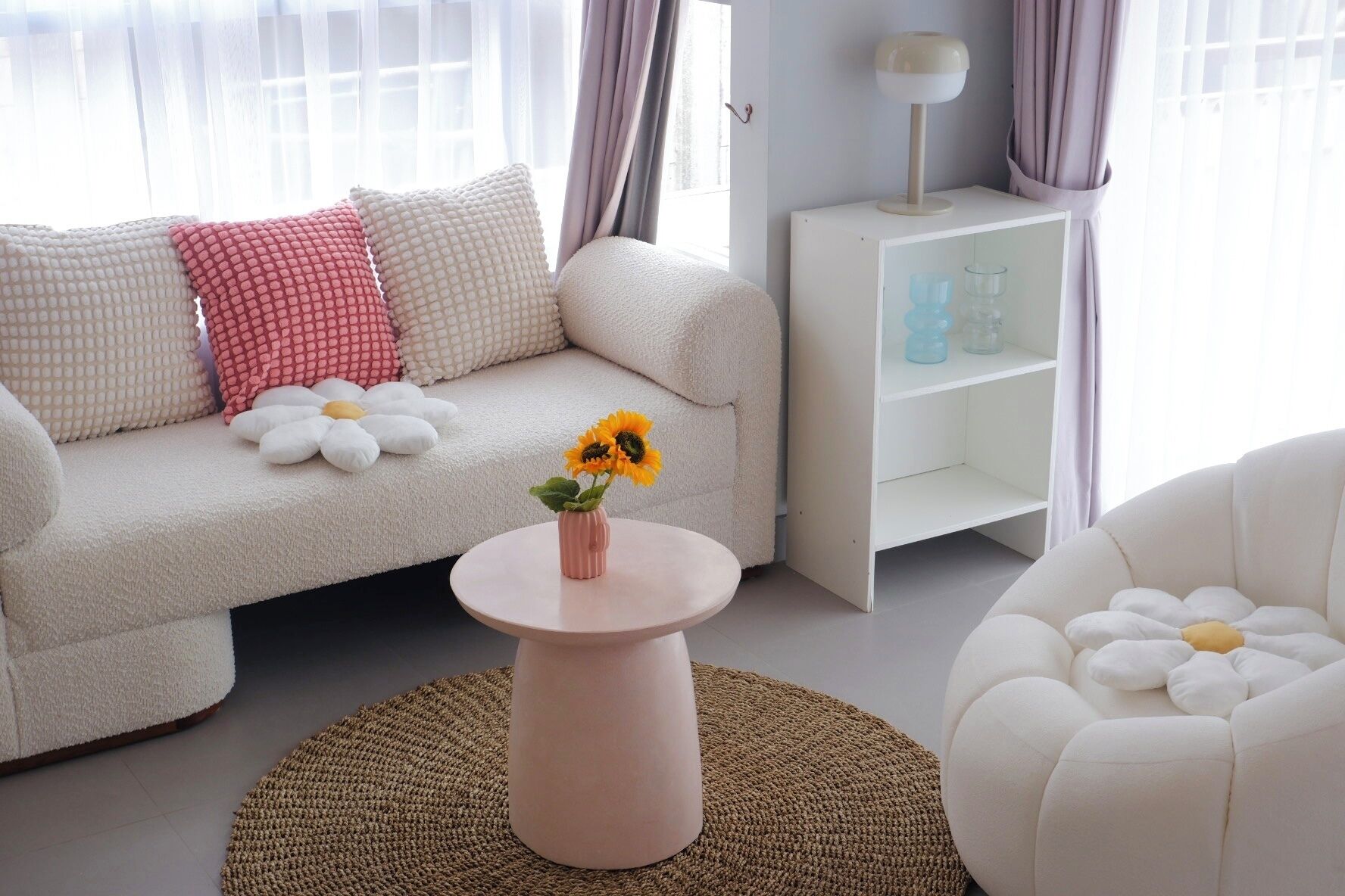 Un salon moderne avec un canapé blanc, une table basse ronde ornée d’un vase de tournesols et un fauteuil blanc.