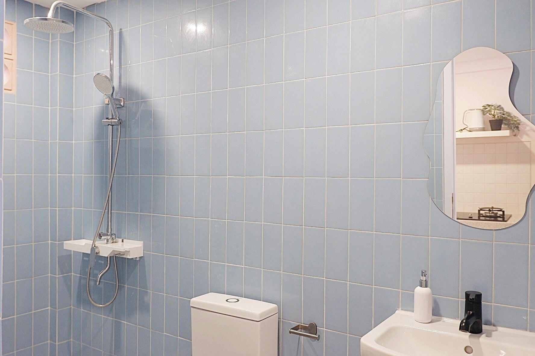 A bathroom with blue tiles, a shower, a toilet, a sink, and a mirror.