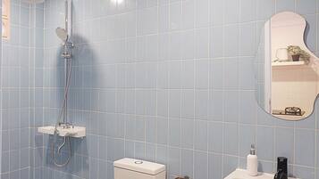 A bathroom with blue tiles, a shower, a toilet, a sink, and a mirror.