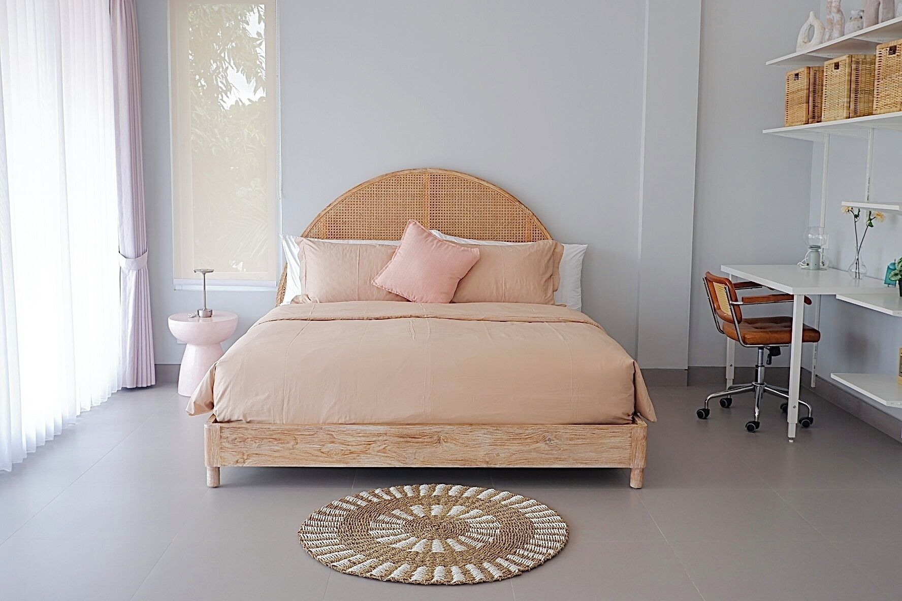 A bedroom with a bed, bedside table, chair, and a round woven rug.