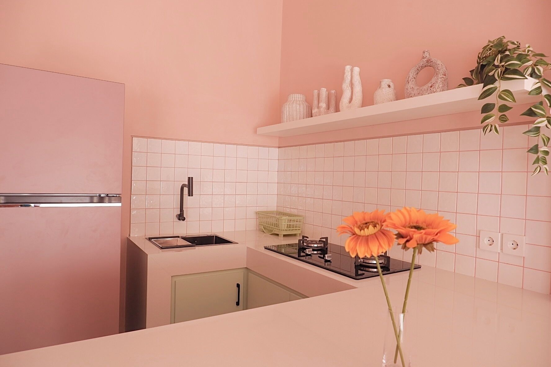 A kitchen with a pink refrigerator, white tiled backsplash, and a small shelf with decorative items.