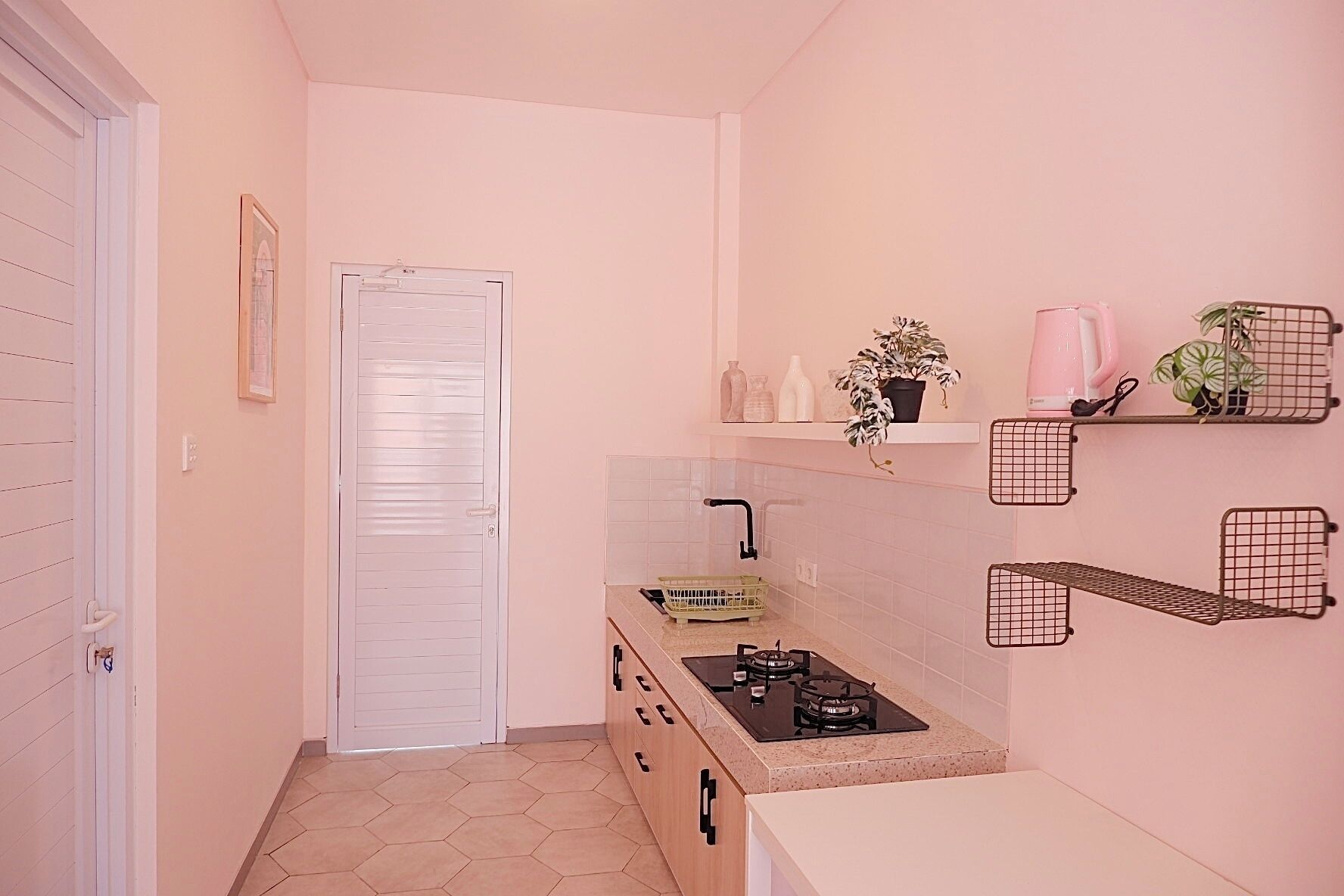 A narrow hallway with a white door, a small kitchen area with a gas stove, and a tiled floor.
