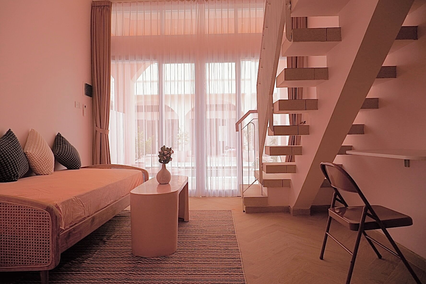 A modern bedroom with a bed, a small round table with a vase, a chair, and a staircase.