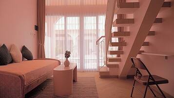 A modern bedroom with a bed, a small round table with a vase, a chair, and a staircase.