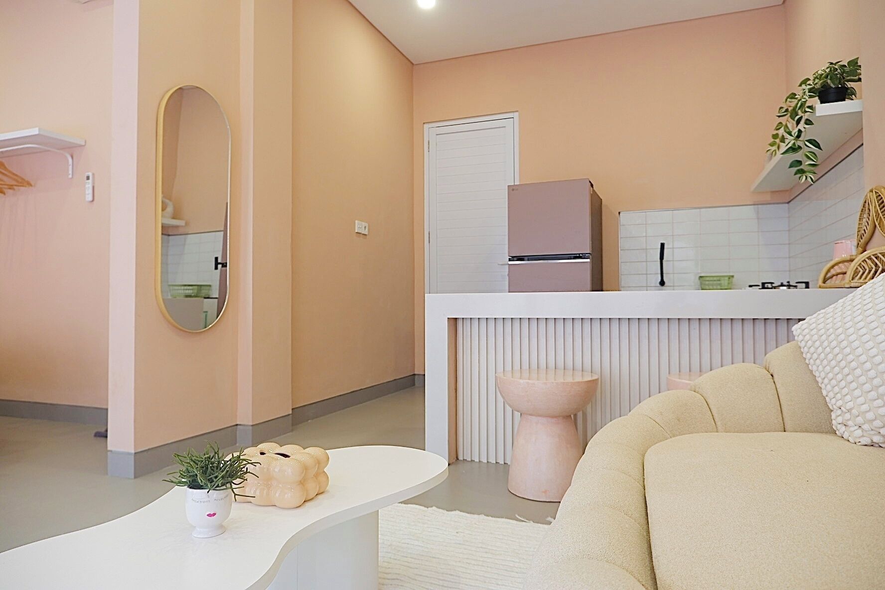 A modern, compact living space with a kitchenette, a sofa, a coffee table, and a mirror.