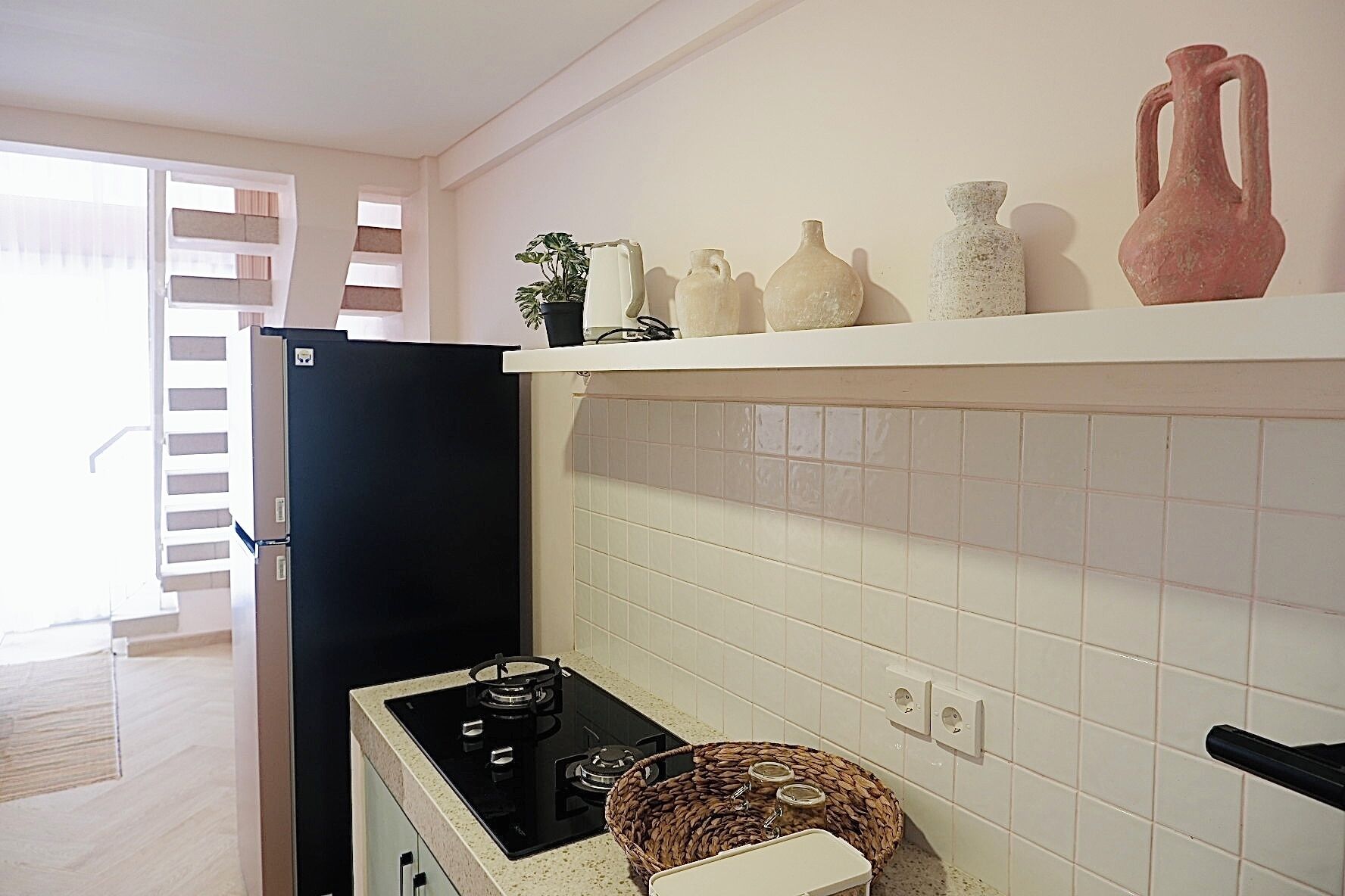 Una cucina con un frigorifero nero, un fornello e uno scaffale con vasi decorativi.