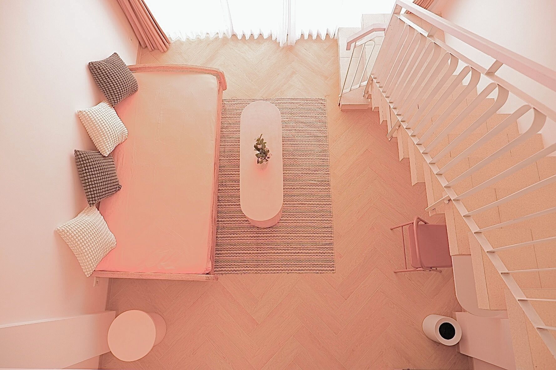 A modern interior with a herringbone floor, a staircase, and a seating area with cushions and a small table.