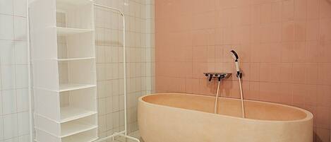 A bathroom with a large bathtub, a white shelving unit, and a pink tiled wall.