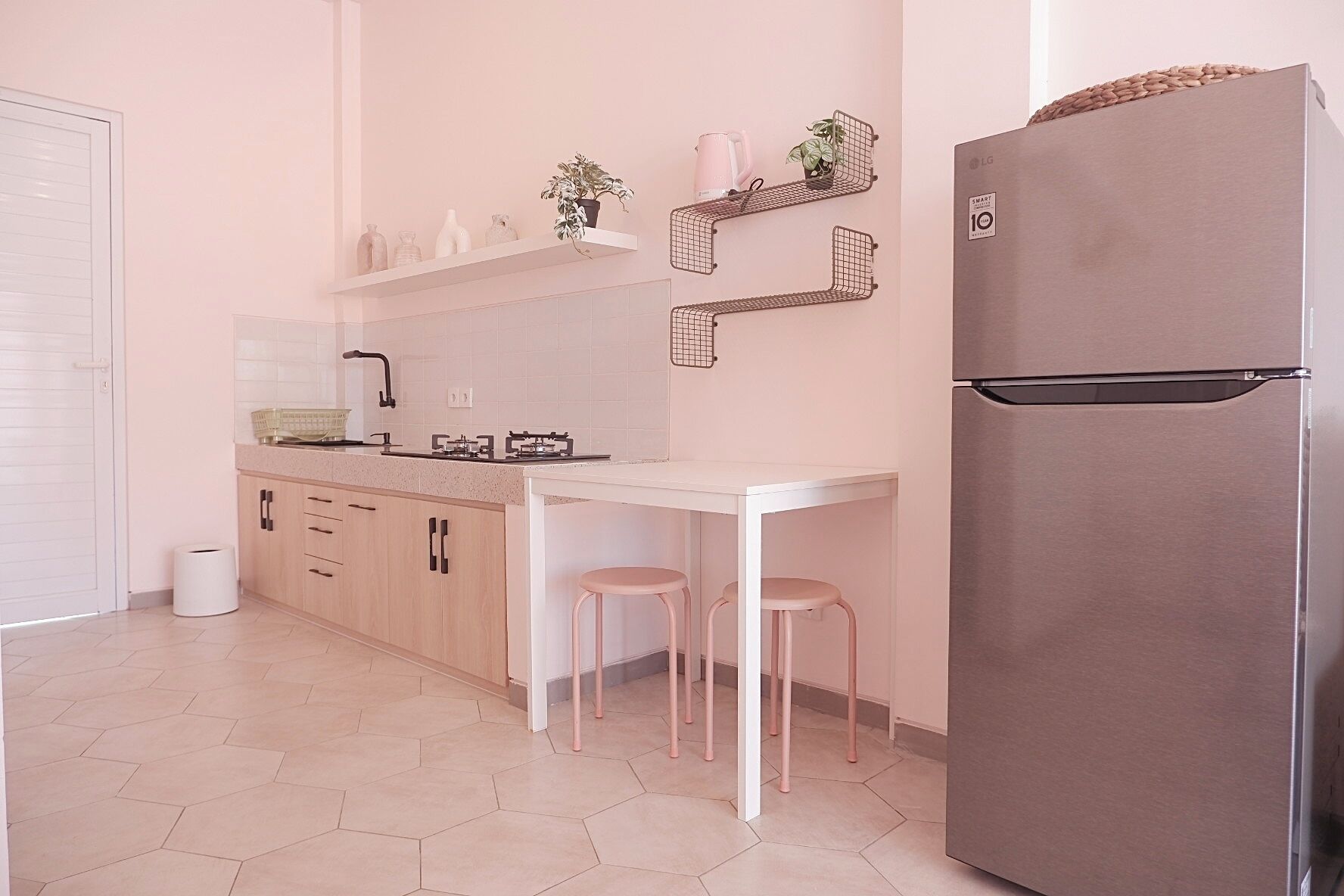 A modern kitchen with a stainless steel refrigerator, a white countertop, and a small dining table with two stools.