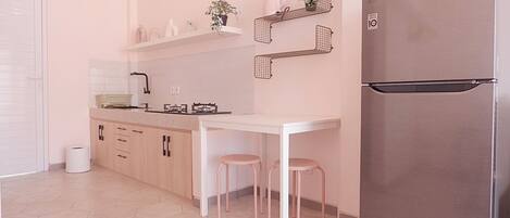 A modern kitchen with a stainless steel refrigerator, a white countertop, and a small dining table with two stools.