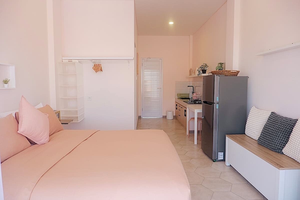 A bedroom with a bed, a desk, and a kitchenette.