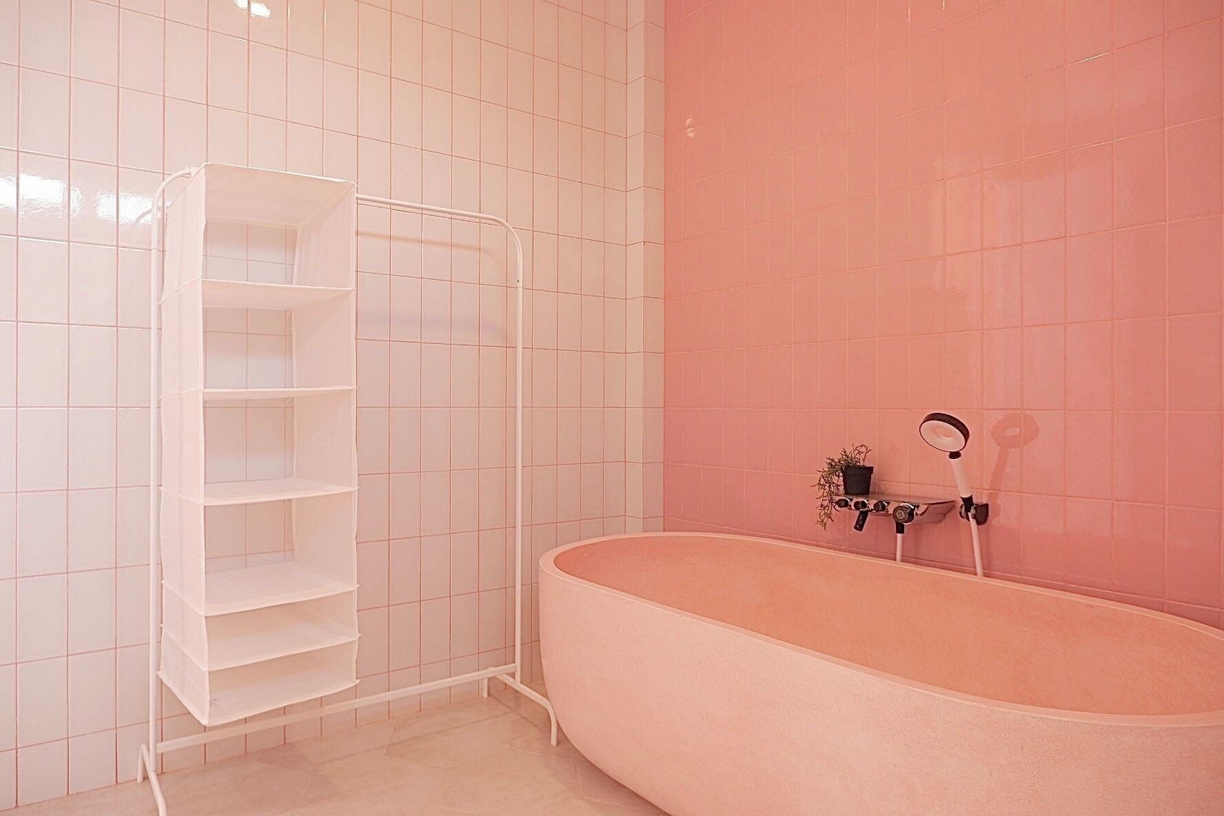 A bathroom with a white tiled wall, a pink bathtub, and a white shelving unit.