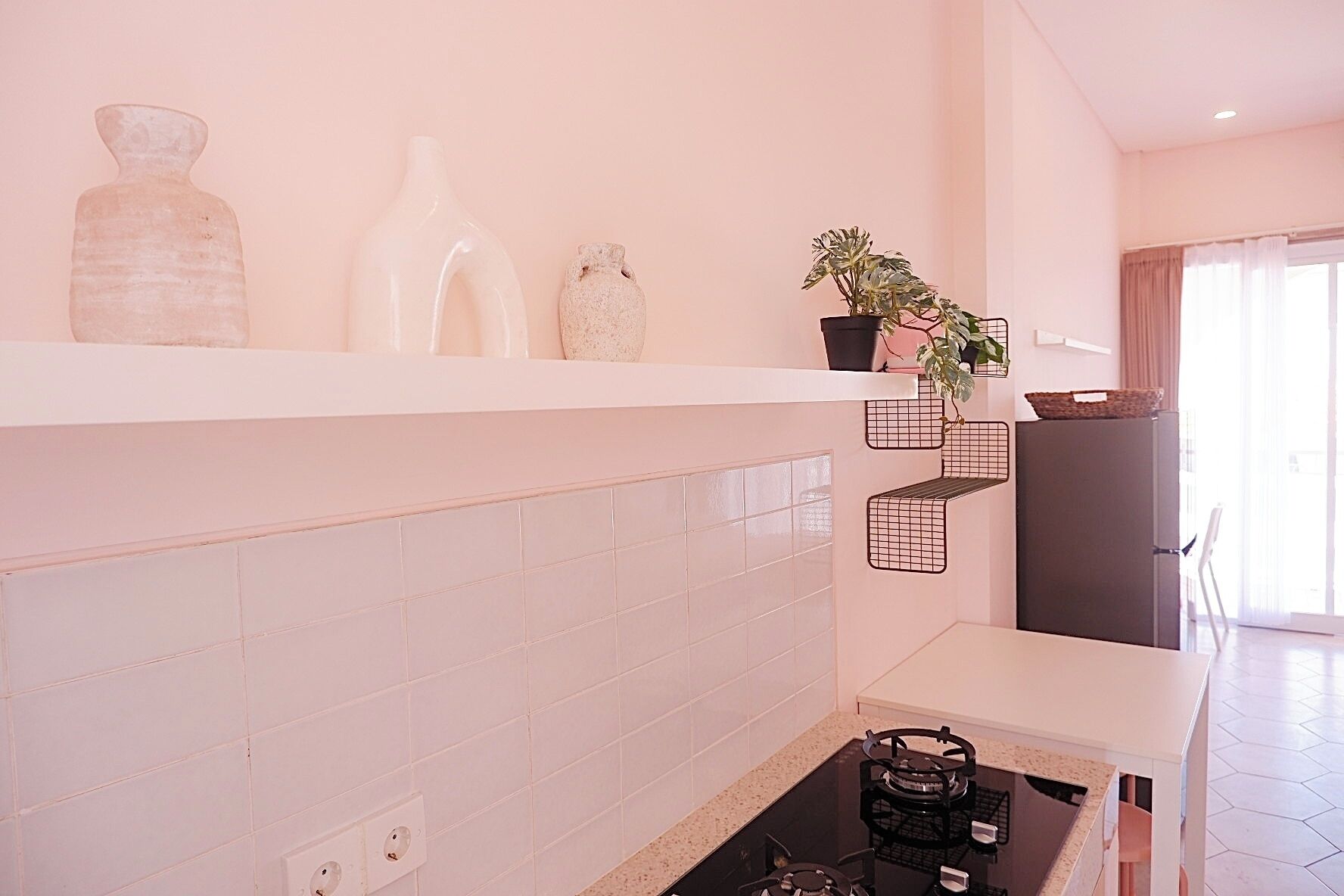 Una cucina moderna con piastrelle bianche, un fornello a gas e un frigorifero. Sul piano di lavoro ci sono vasi decorativi e una pianta in vaso.