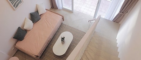 A bedroom with a bed, pillows, a small table, and a view of a balcony.