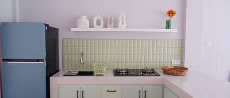 Una cocina con un refrigerador azul, un lavamanos blanco, una estufa a gas y un salpicadero de azulejos verdes.
