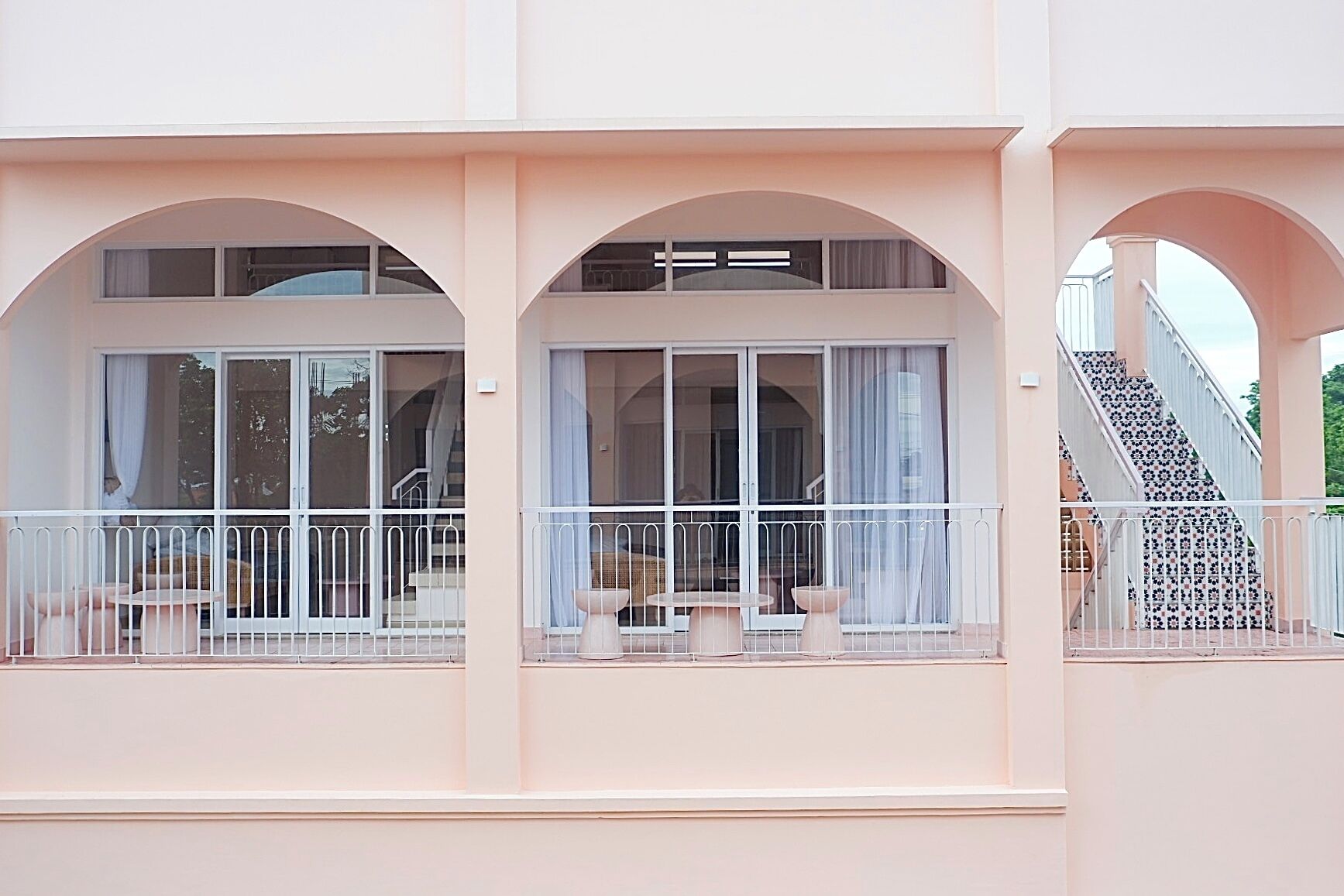 A building with large arched windows, a balcony with a white railing, and a staircase with patterned tiles.