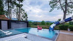 A swimming pool with a slide, a pink flamingo float, and a lounge area with a patterned table. - Khaoyai Valley 3 (Pak Chong)