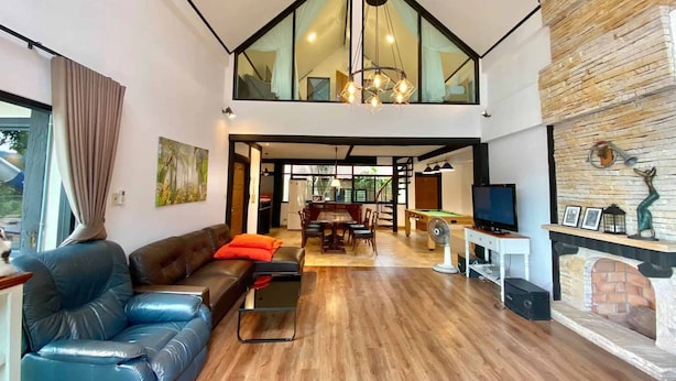 A spacious living area with a high ceiling, a wooden floor, a leather sofa, a dining table, and a television. - Khaoyai Valley 3 (Pak Chong)