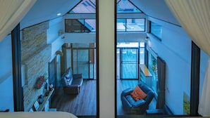 A bedroom with a large window, a bed, and a view of a living area with a sofa and a chair. - Khaoyai Valley 3 (Pak Chong)