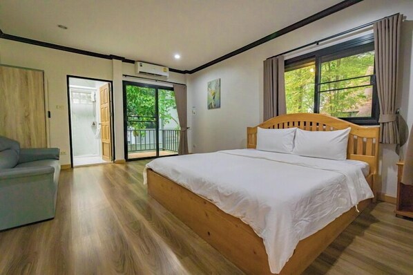 A bedroom with a wooden bed, a grey sofa, and a sliding glass door leading to a balcony.