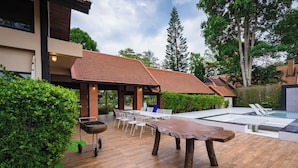 A modern outdoor patio with a wooden table, white chairs, and a pool area. - Khaoyai Valley 3 (Pak Chong)