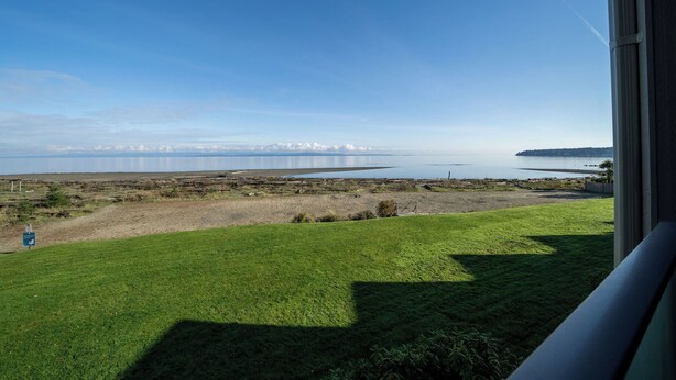 A view from a window overlooking a grassy area with a body of water and distant mountains.