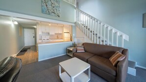 A modern living room with a brown sofa, a white coffee table, and a staircase leading to an upper level.