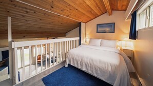 Une chambre avec un plafond en bois, un lit avec une literie blanche, deux lampes de chevet et une fenêtre avec des rideaux.